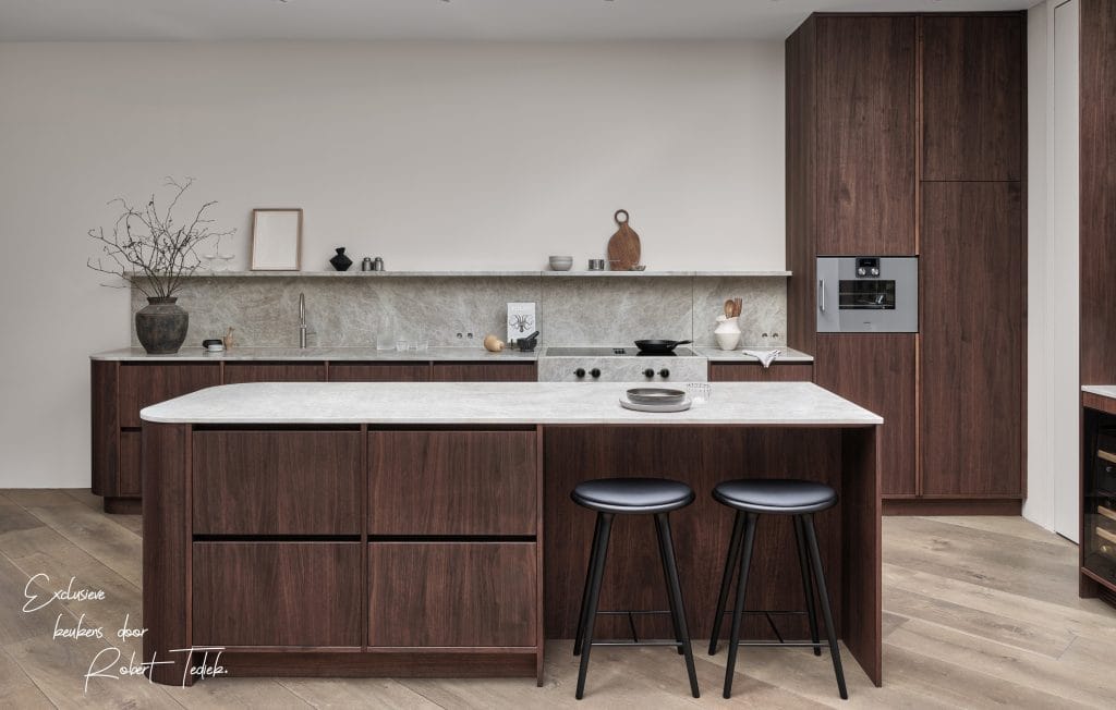 Notenhouten keuken met een minimalistische en elegante uitstraling, waar in het design gebruik is gemaakt van een natuurstenen blad en luxe details. In combinatie met de verfijnde rondingen zorgt het voor een stijlvol geheel.